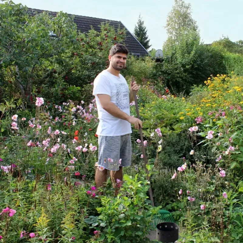 Medarbetare med räfsa bland blommor i en frodig trädgård