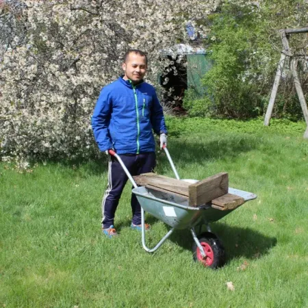 Medarbetare kör skottkärra med virke i en blommande trädgård