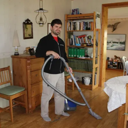 Medarbetare dammsuger ett vardagsrum med bokhylla och gammaldags lampor